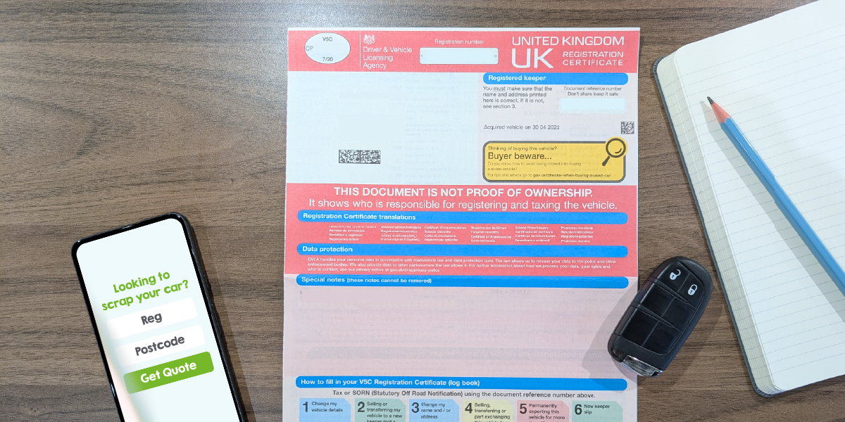 Photo of a V5C registration document, a phone showing a scrap car quote form and a set of car keys all on a wooden table top