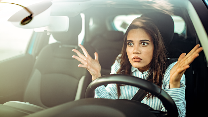 Person behind steering wheel of car with arms up looking stressed