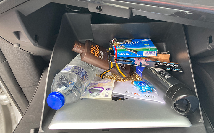Photo of items in a glovebox including sun cream, water, cash