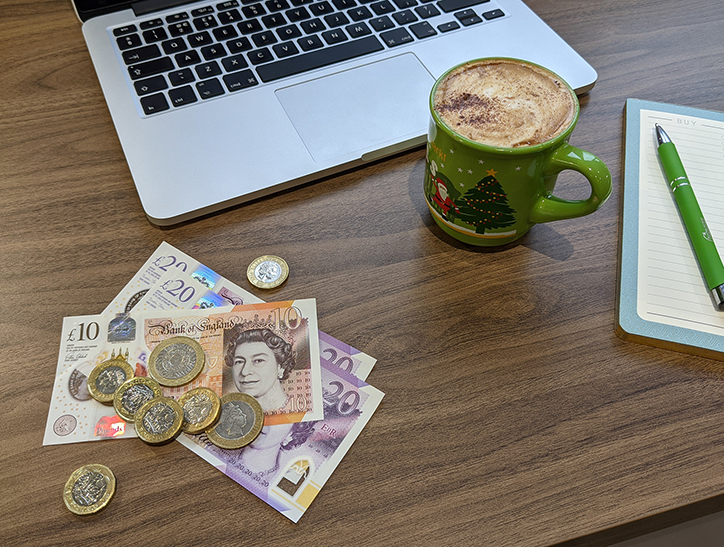 Cash on a table with laptop, notepad and a festive coffee