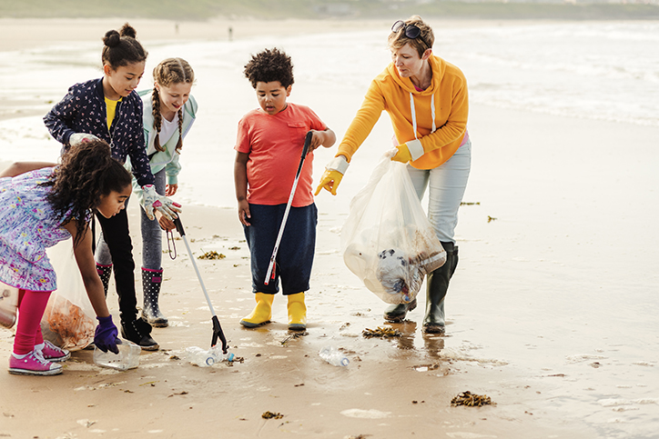 Collecting rubbish off a beach. Plastic containers, bottles in their bag. They are using a mechanical grabber. Woman working with children to clean up the beach to help the environment and marine life