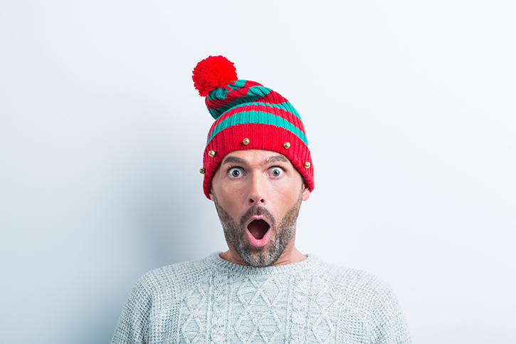 Funny christmas portrait of showcked man wearing elf cap. Man wearing winter sweater standing against white background.