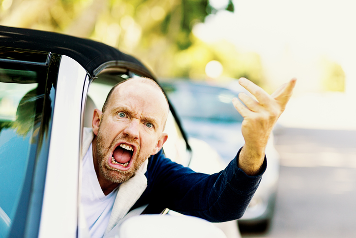 A furiously angry male driver grimaces, gesturing threateningly through the car window in a bout of road rage!