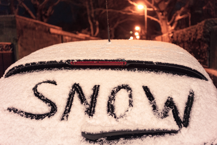 The word snow written in the snow, on the rear window of a car, parked at night.