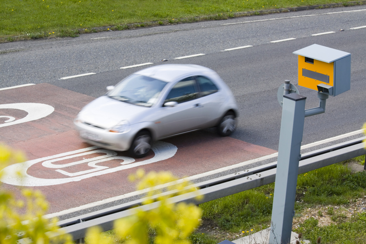 A UK speed camera monitors the speed of a passing car in a 50mph zone. Motion blur on car.