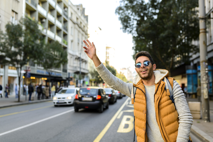 Person with orange jacket and sunglasses stopping taxi in the city street