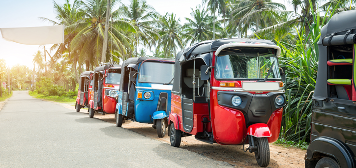 Colourful tuk tuks lines on the edge of a street with palm trees