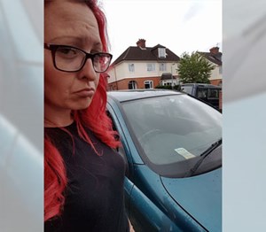 Woman with red hair looking sad stood with her old car