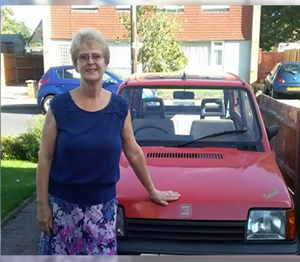 Woman stood with her old red car, smiling
