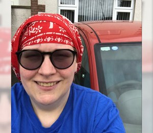 Person wearing sunglasses smiling with a red car in the background