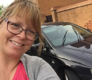 Woman smiling, in the background is a black car
